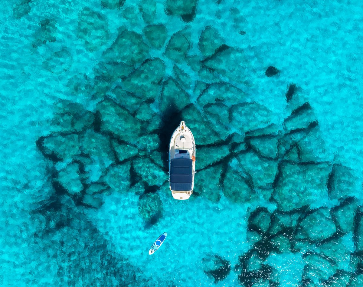 Aerial drone view of white boat anchored above rocky seabed in shallow turquoise sea