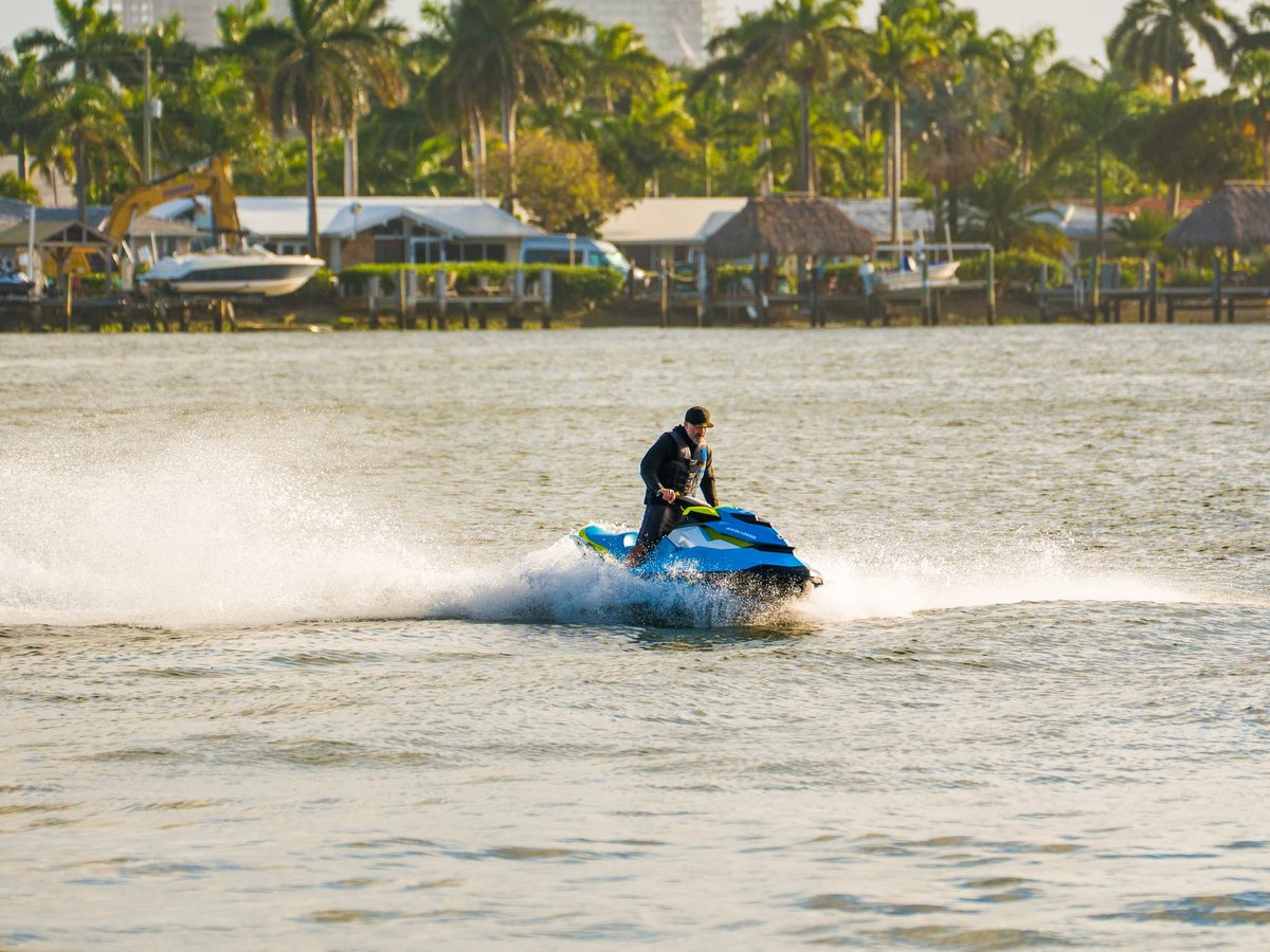 A man wearing a life vest rides a blue and yellow jet ski creating white water spray