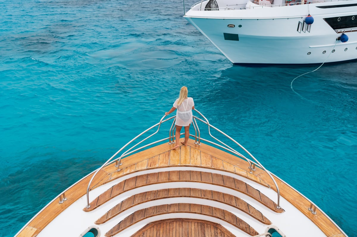 Woman on bow of luxury yacht over turquoise water