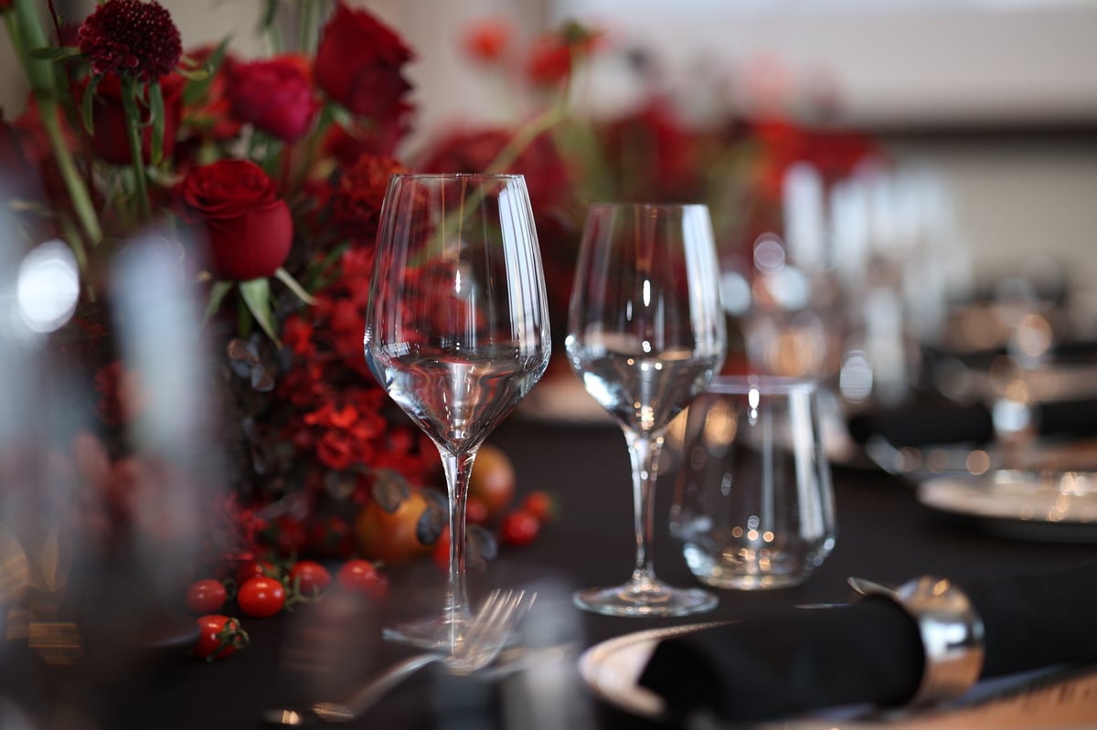 Upscale dining table with crystal wine glasses, black napkins, polished cutlery and vibrant red floral centerpiece