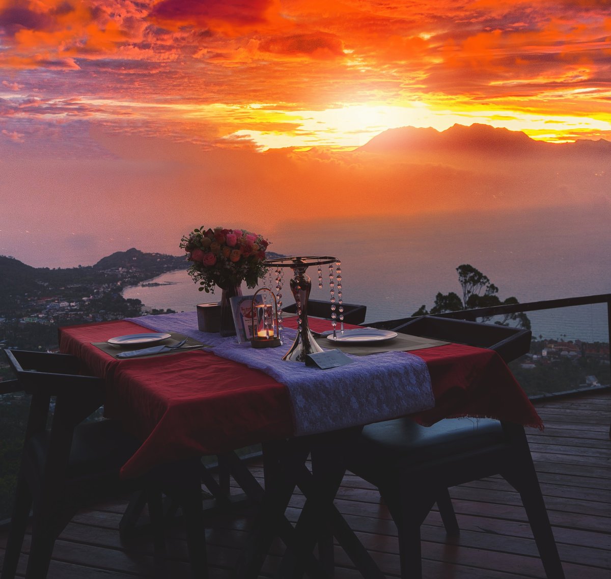 Outdoor dining table set with candles overlooking a coastal landscape at sunset