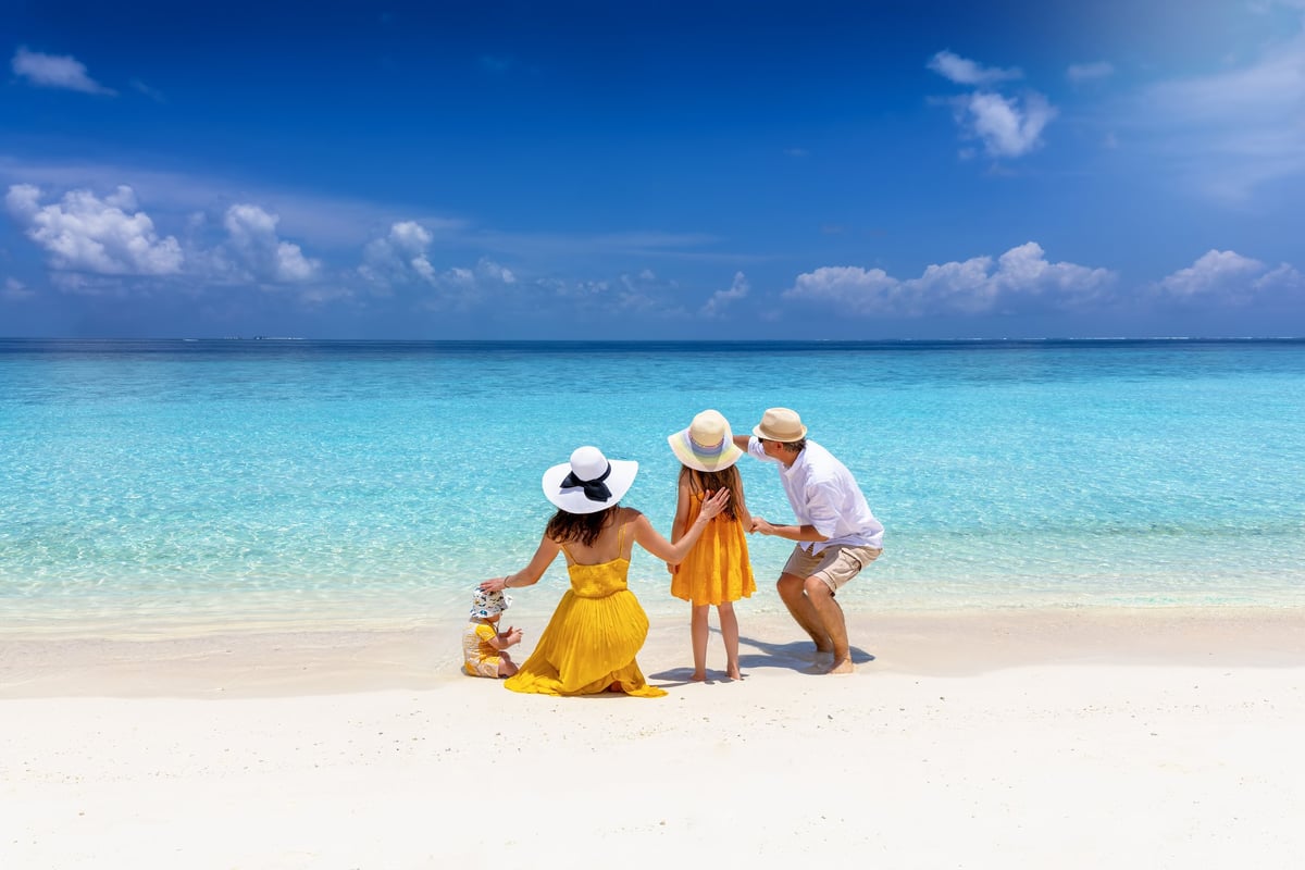 A elegant family of four stand on a tropical paradise beach and enjoys the turquoise ocean and sunshine