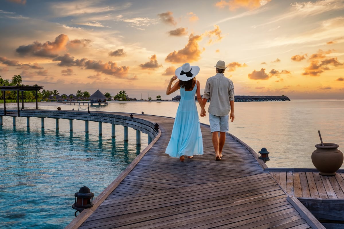 A couple walks holding hands over a pier in the tropical Maldives islands during their romantic vacations