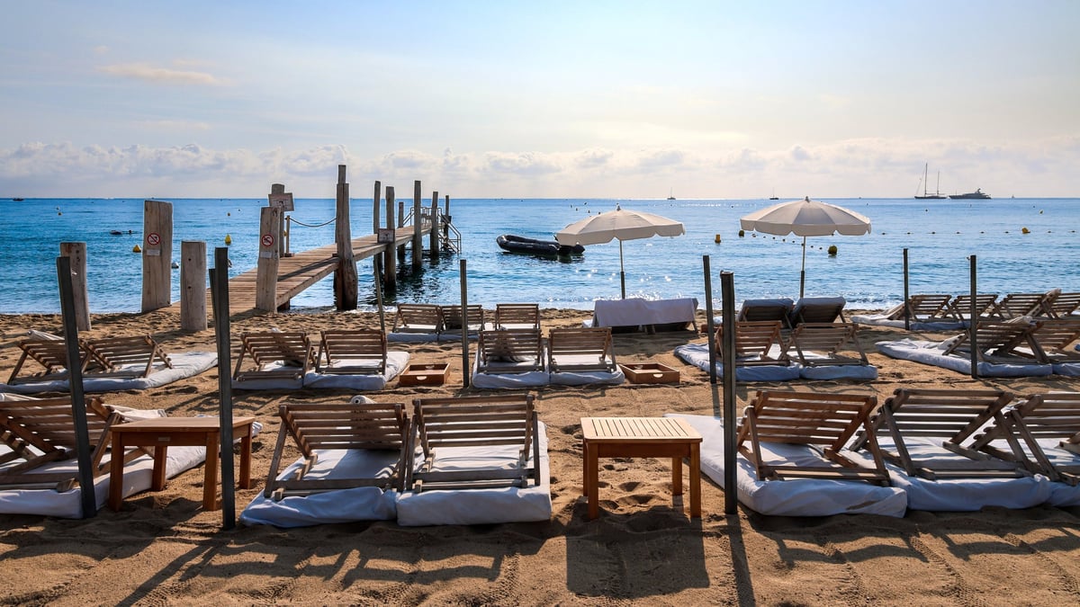 Empty luxury beach club with rows of wooden sun loungers and white umbrellas facing a calm turquoise sea at Pampelonne Beach in Saint-Tropez
