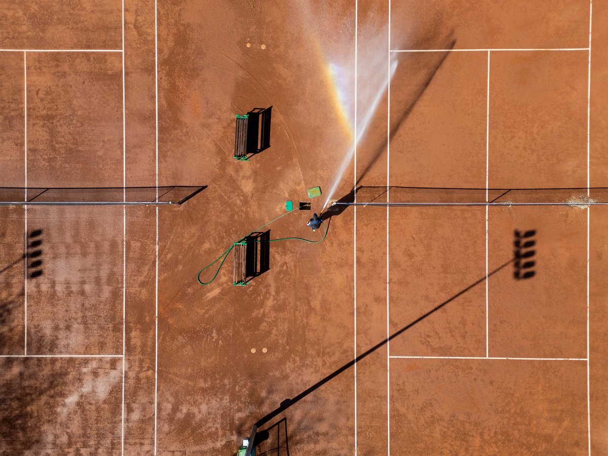 Top-down aerial drone shot of red clay tennis courts being watered