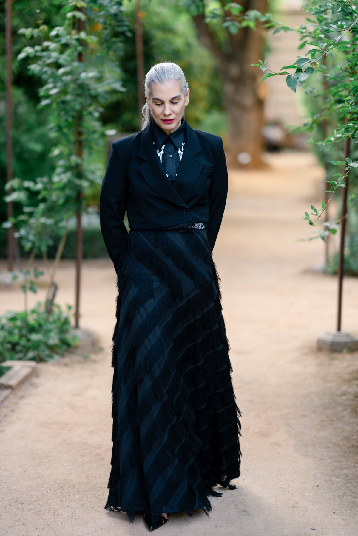 Closeup of senior woman in black gown, creative director portrait with confident gaze, high-contrast lighting, minimal makeup, statement brooch, tailored collar