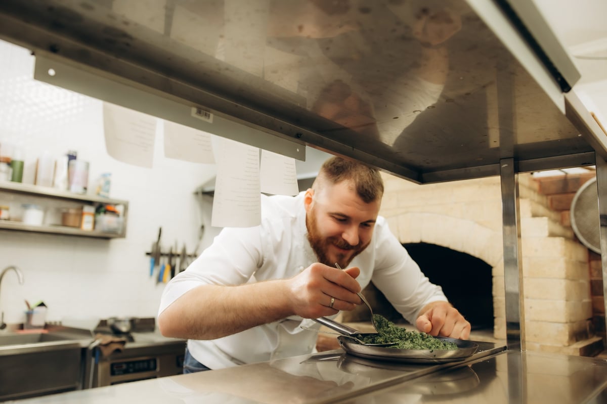 Chef working in a commercial kitchen, carefully plating a dish with a spoon