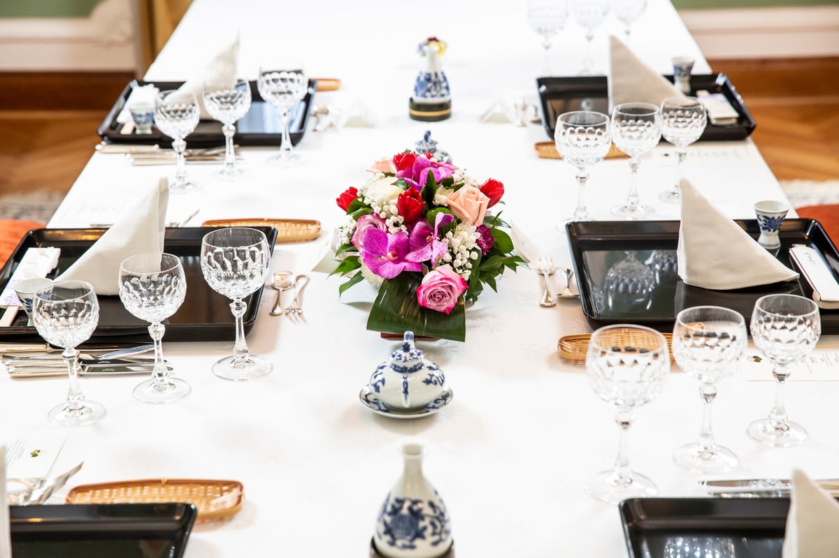 An elegantly arranged dining table with a white tablecloth, crystal glasses and a colorful flower arrangement with roses