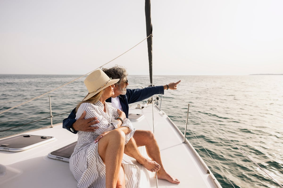 Mature adult couple relaxing on a sailboat, man pointing into the ocean
