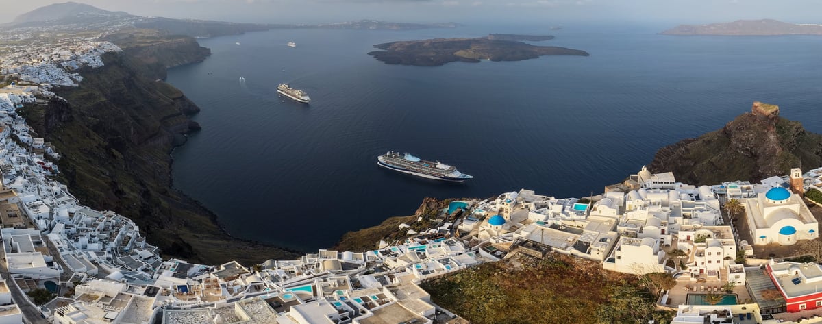 Sweeping panorama of Santorini's whitewashed cliffside villages, blue-domed churches, and cruise ships in the caldera