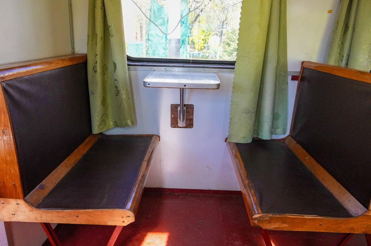 Train carriage interior featuring two wooden benches with dark cushions
