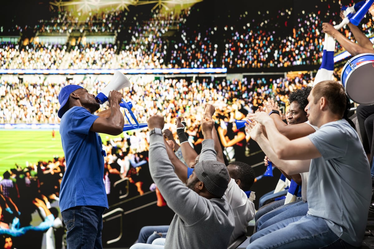 Excited football fan leader using bullhorn to unite blue supporter group in stadium stands during live soccer match atmosphere