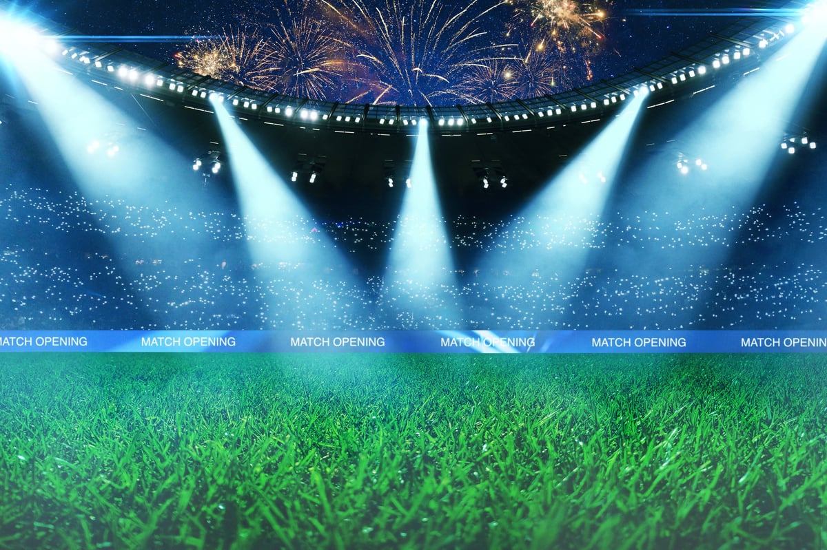 Empty green soccer field of a huge stadium with bright spotlights, fans in the stands and spectacular fireworks in the night sky