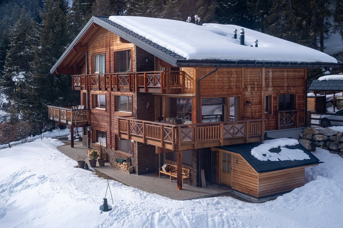 Modern luxury chalet with wooden facade and snow-covered roof among forest in winter in Crans-Montana Switzerland