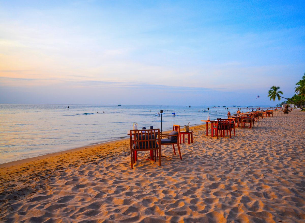 Beachside dining setup at sunset with calm ocean waves and palm trees