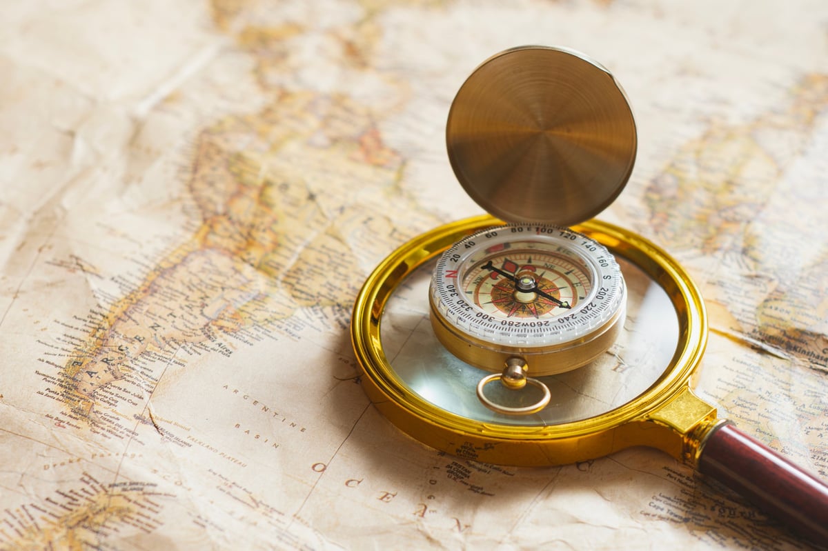 Magnifying glass and compass placed on vintage world map representing navigation, research, and travel planning