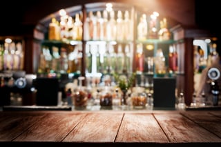 Empty rustic wooden table top or bar counter with glowing bokeh lights and liquor bottles
