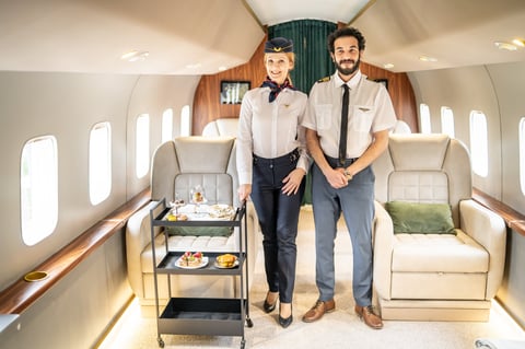 Two flight attendants stand inside a private jet cabin while serving snacks and drinks