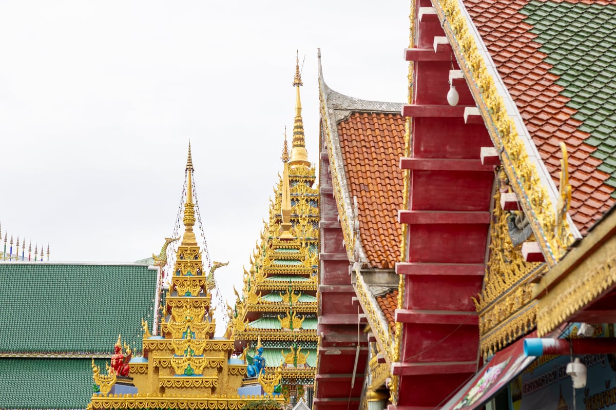 Intricate golden spires and decorative elements adorning the multiple tiered roofs of a traditional Thai Buddhist temple