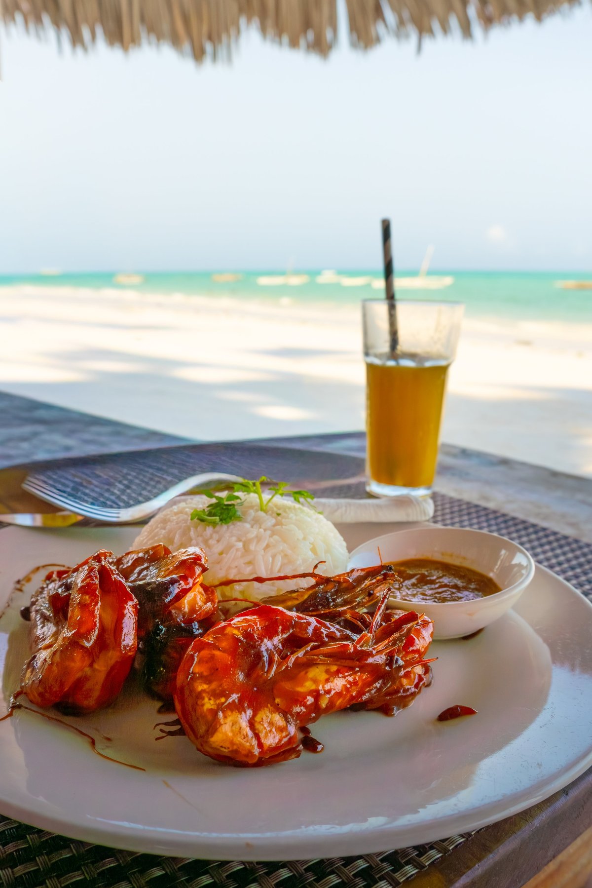 Close up plate grilled giant prawns rice sauce tall glass tropical juice