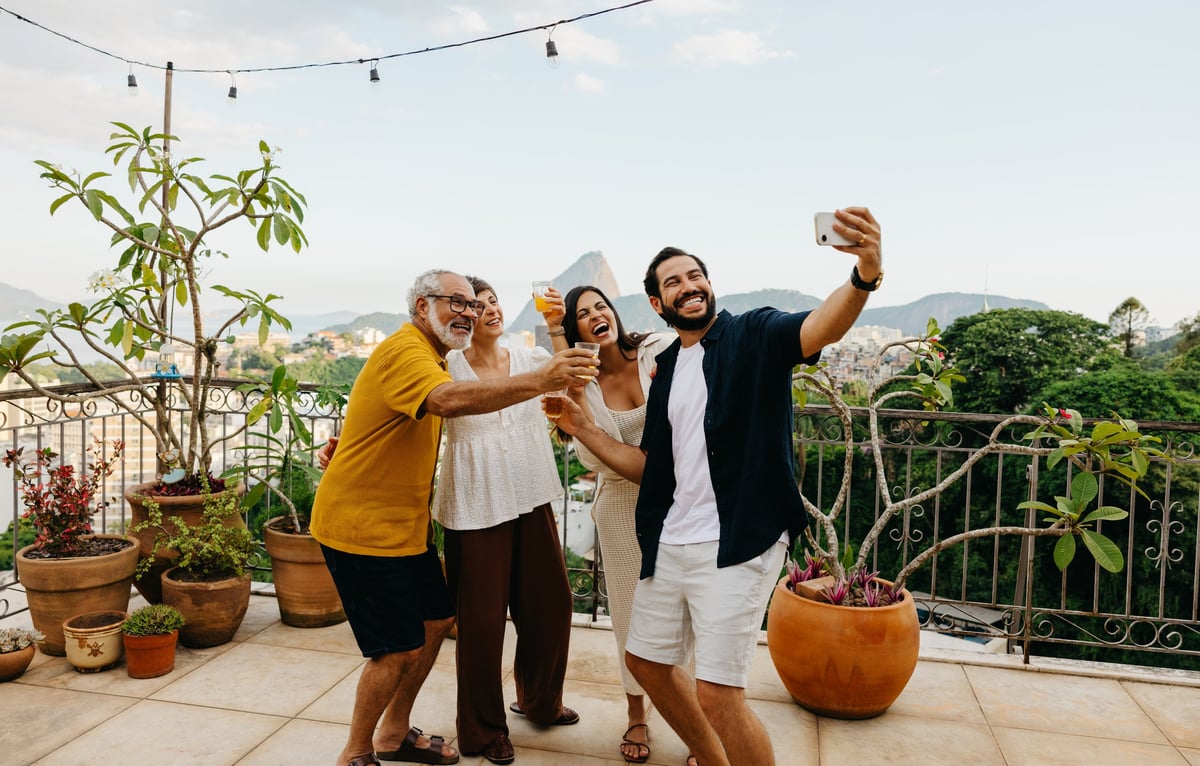 A family gathers on a patio overlooking a lush landscape, smiling and taking a cheerful selfie