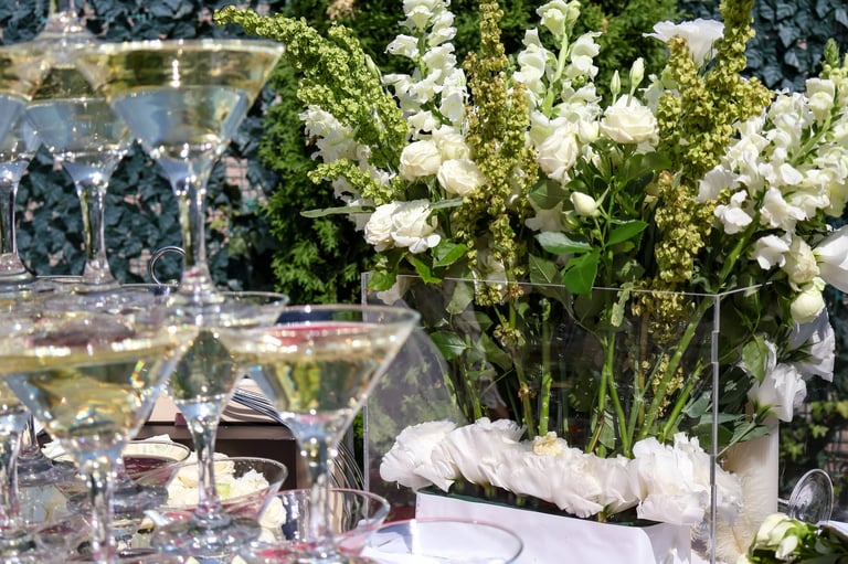 Pyramid of martini glasses filled with champagne against white flowers at an outdoor wedding