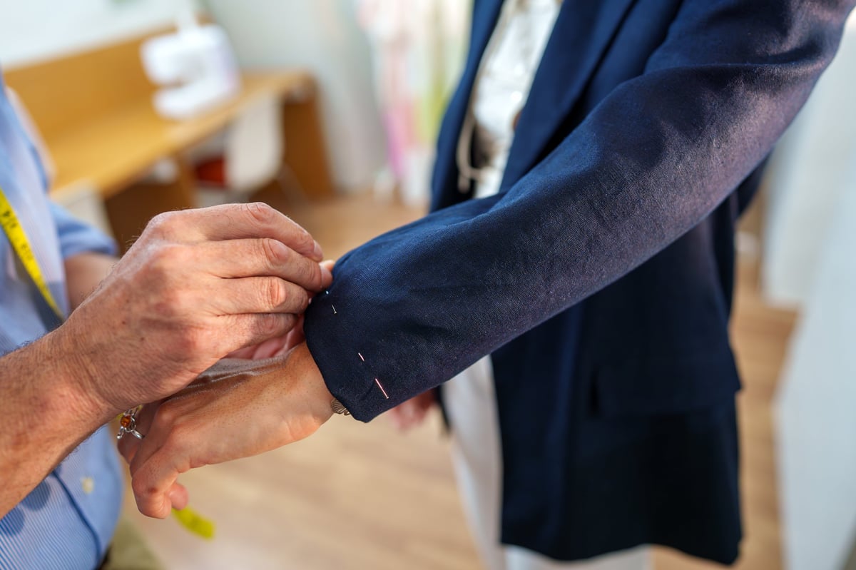 Experienced tailor adjusting the sleeve length of a navy suit jacket for a customer in a professional fashion atelier