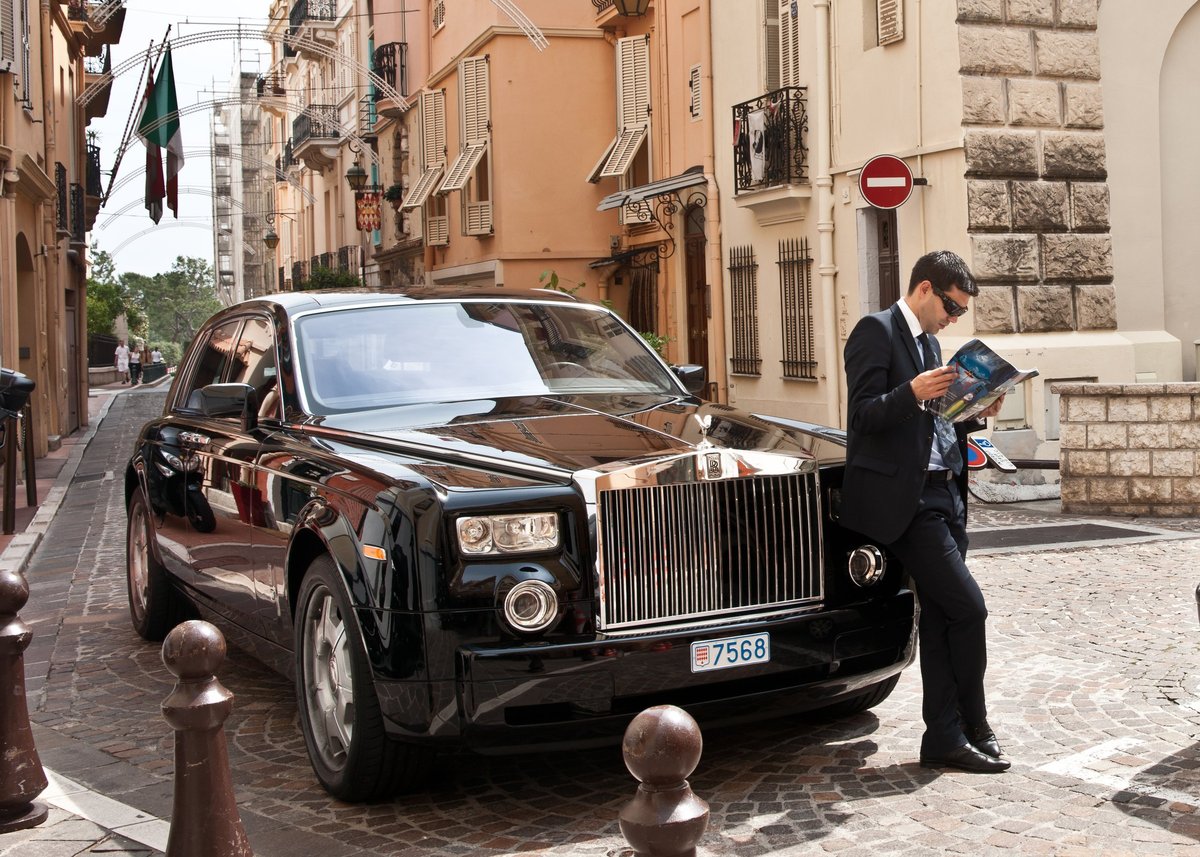 Chauffeur stands by black Rolls Royce car in Monaco street