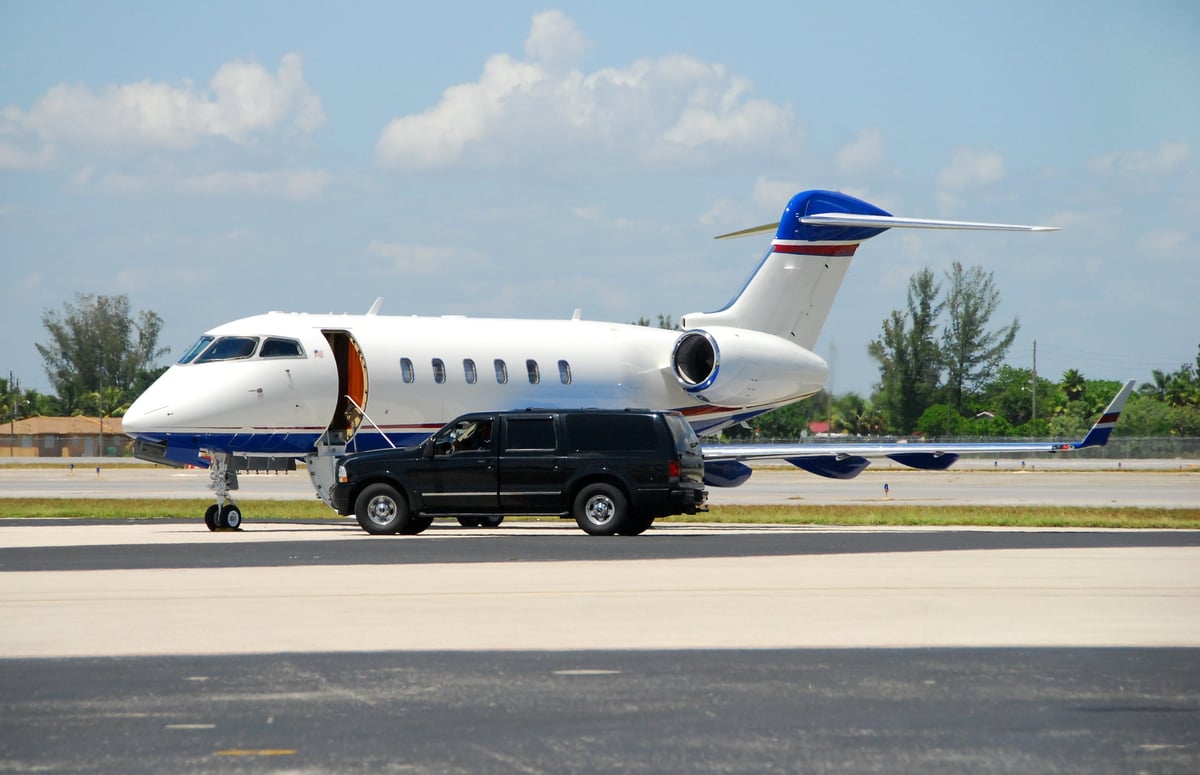 A private jet parked on the tarmac with an SUV parked nearby