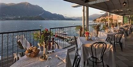 Waterfront restaurant terrace with dining tables overlooking a lake and mountains at sunset