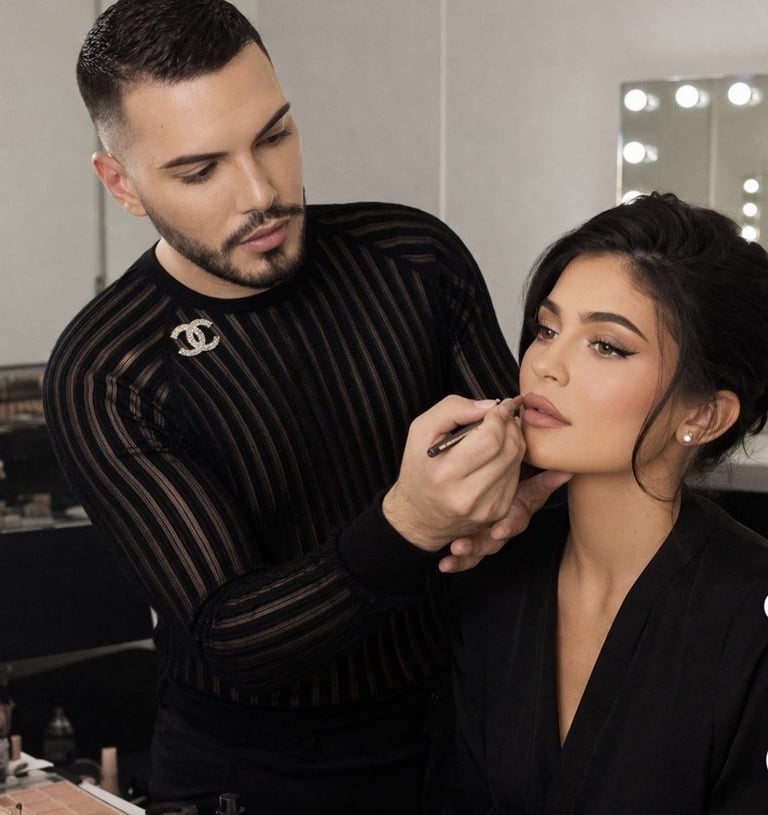 Professional makeup artist applies eyeshadow to female client in studio with illuminated mirror in background