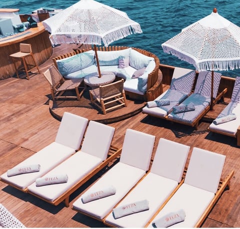 Luxury yacht deck with lounge chairs, woven seating areas, white umbrellas, and ocean views