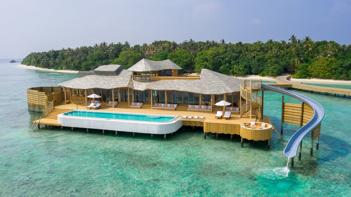 Luxury overwater bungalows with wooden decking and pools in turquoise tropical waters, forest-covered island in background