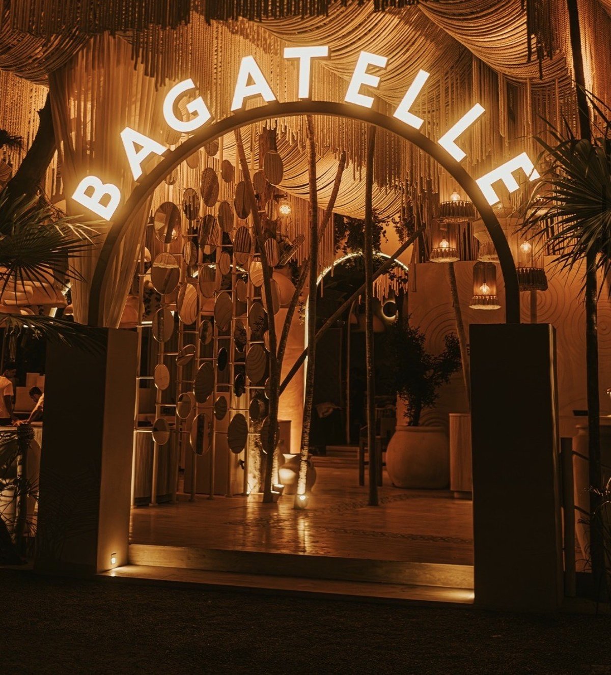 Illuminated bagel shop entrance with neon sign, wooden facade, hanging decorations, and warm golden lighting at night