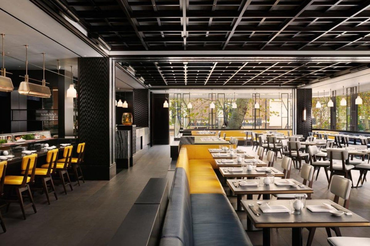 Modern restaurant interior with yellow chairs, wooden tables, black walls, and industrial ceiling with pendant lighting