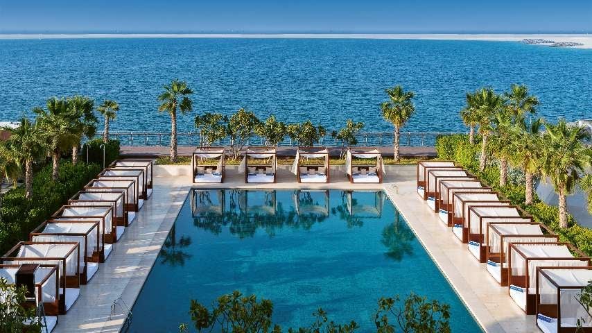 Luxury resort pool overlooking the sea with lounge chairs and palm trees on a sunny day