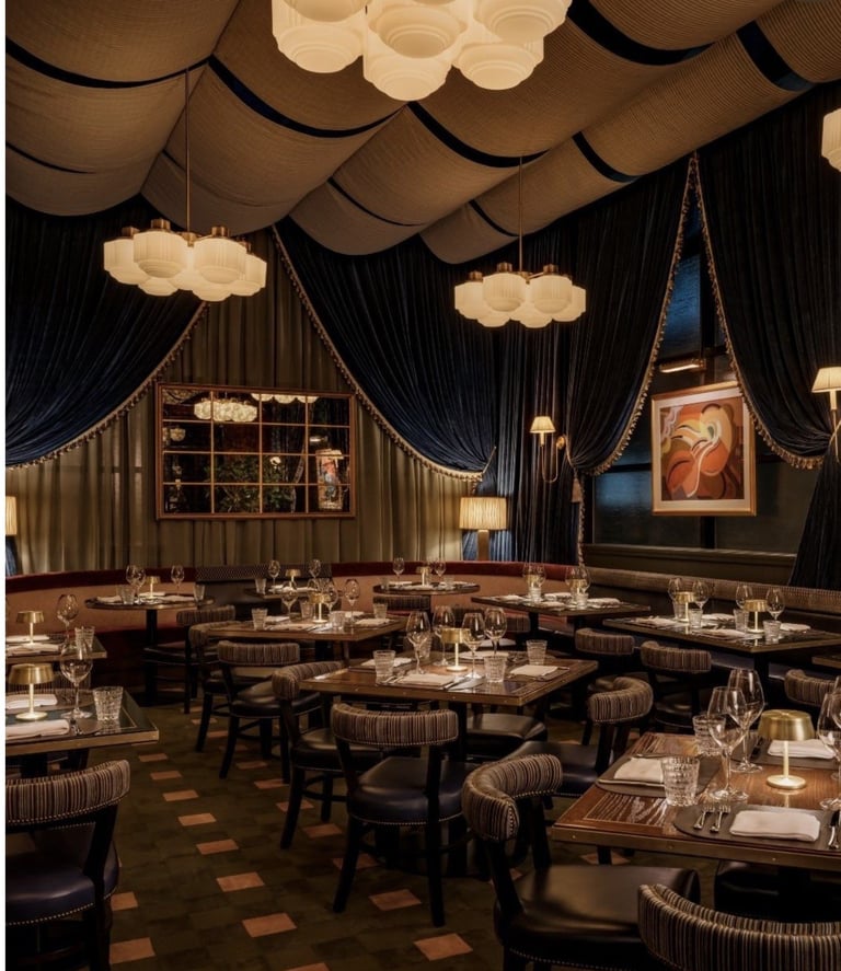 Elegant upscale restaurant dining room with draped black curtains, cream cloud-shaped pendant lights, and round tables set with place settings