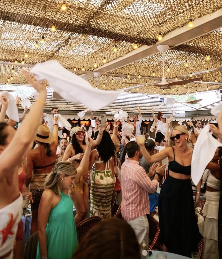 Crowd of people at an indoor party or celebration dancing and waving white fabric under a woven ceiling