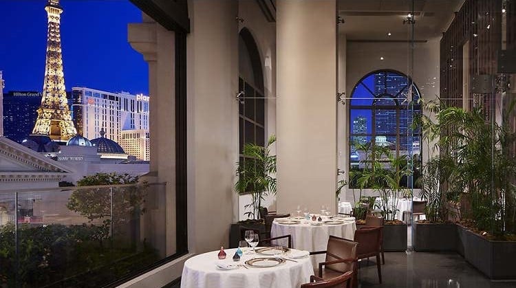 Upscale restaurant dining room with white tablecloth tables, floor-to-ceiling windows overlooking the Eiffel Tower at night in Paris