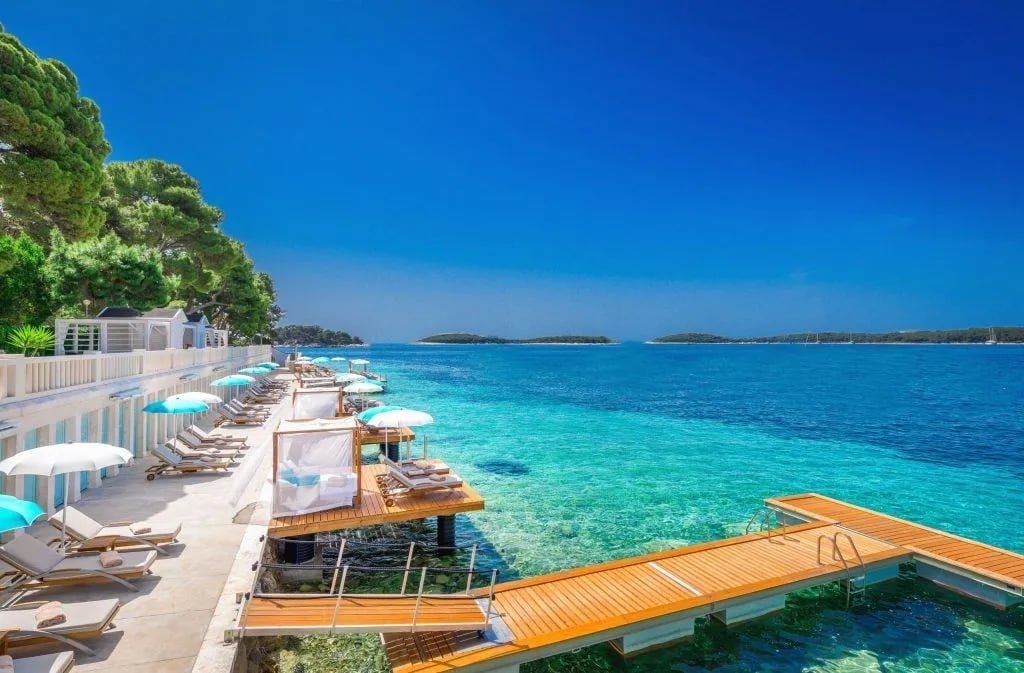 Luxury beachfront villa with wooden dock, sunbeds, and turquoise Mediterranean sea under clear blue sky