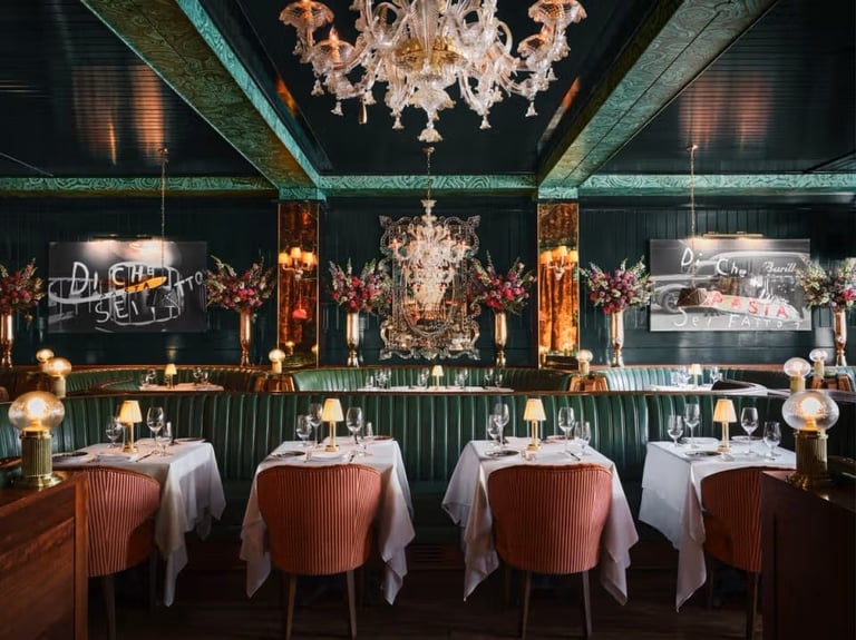Elegant fine dining restaurant interior with tables set with white linens, coral chairs, chandelier, and ornate bar decorated with candles and lighting