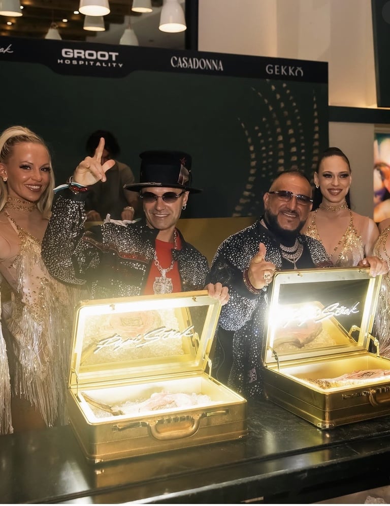 Group of five people in sparkly outfits at an event, standing behind gold display cases with open lids at a table