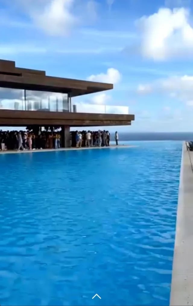 Modern waterfront structure with spectators gathered on an open platform overlooking a bright blue ocean and clear sky