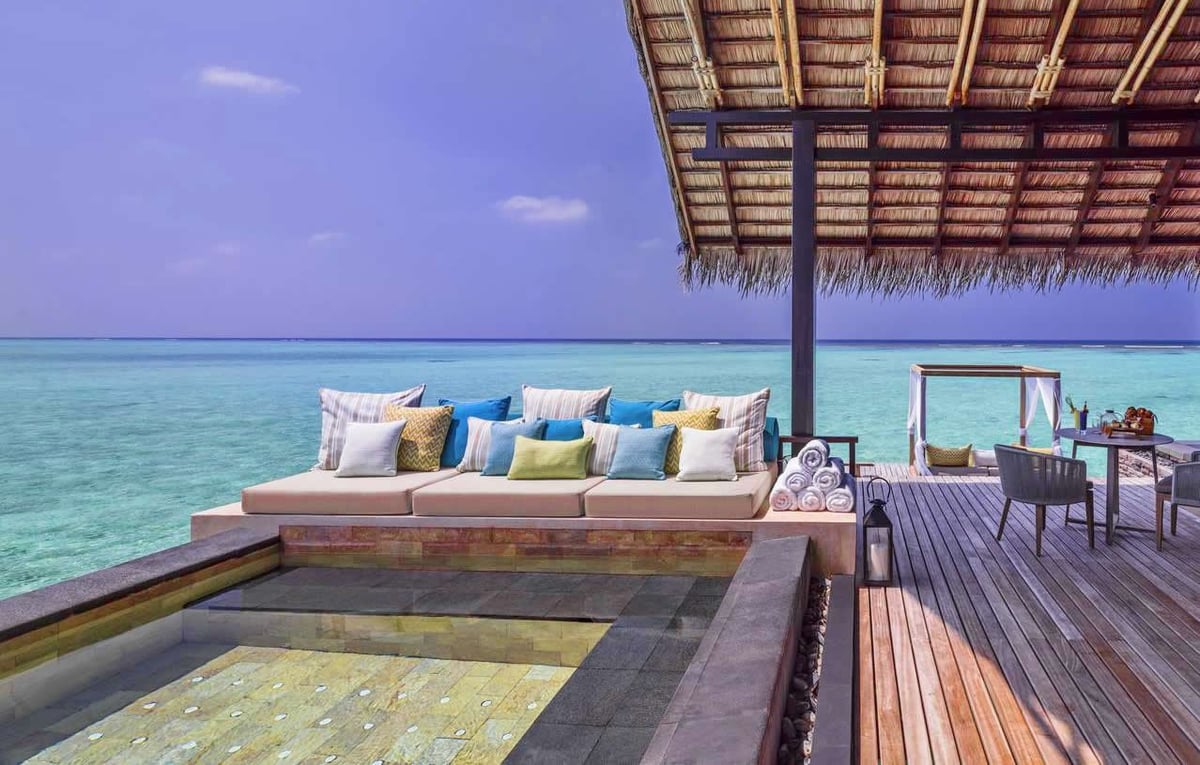 Luxury overwater bungalow with cushioned seating, thatched roof, and turquoise ocean view