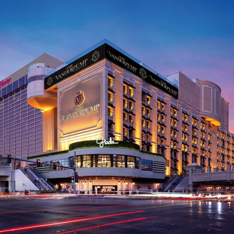 Illuminated luxury hotel building with gold facade and signage at dusk, featuring modern architecture and light trails from passing traffic