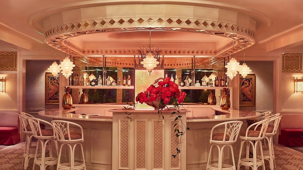 Luxurious pink-toned bar lounge with ornate circular ceiling fixture, decorative shelving, fresh red roses, and cream-colored seating