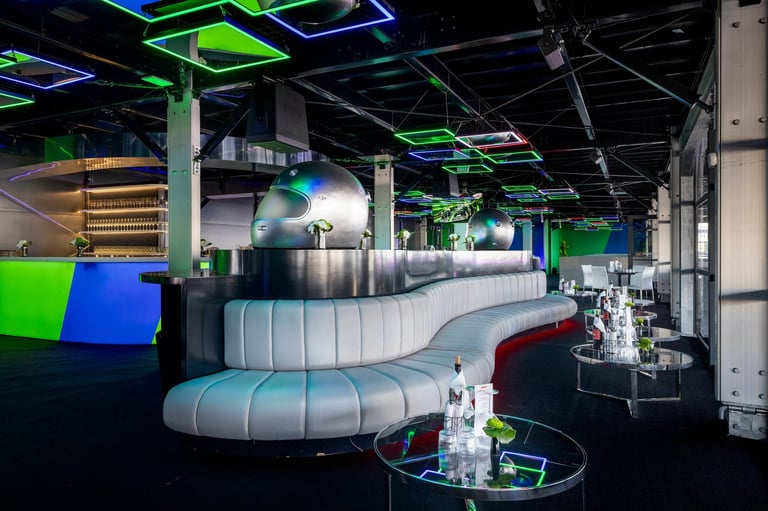 Modern lounge interior with curved white seating pods, neon green ceiling panels, blue accents, and minimalist decor in an industrial warehouse space.