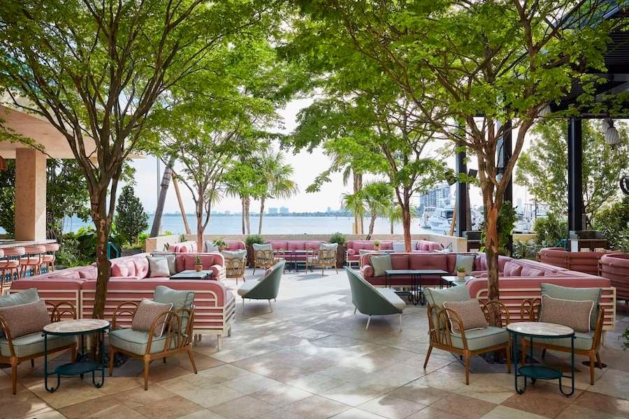 Outdoor lounge area with mid-century modern furniture, large trees, and waterfront views