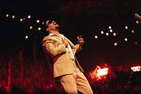 Performer in cream-colored suit on stage under warm stage lights with bokeh lights