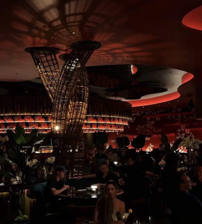 Dimly lit nightclub interior with dramatic red and orange lighting, ornate architectural details, and silhouettes of people socializing at tables